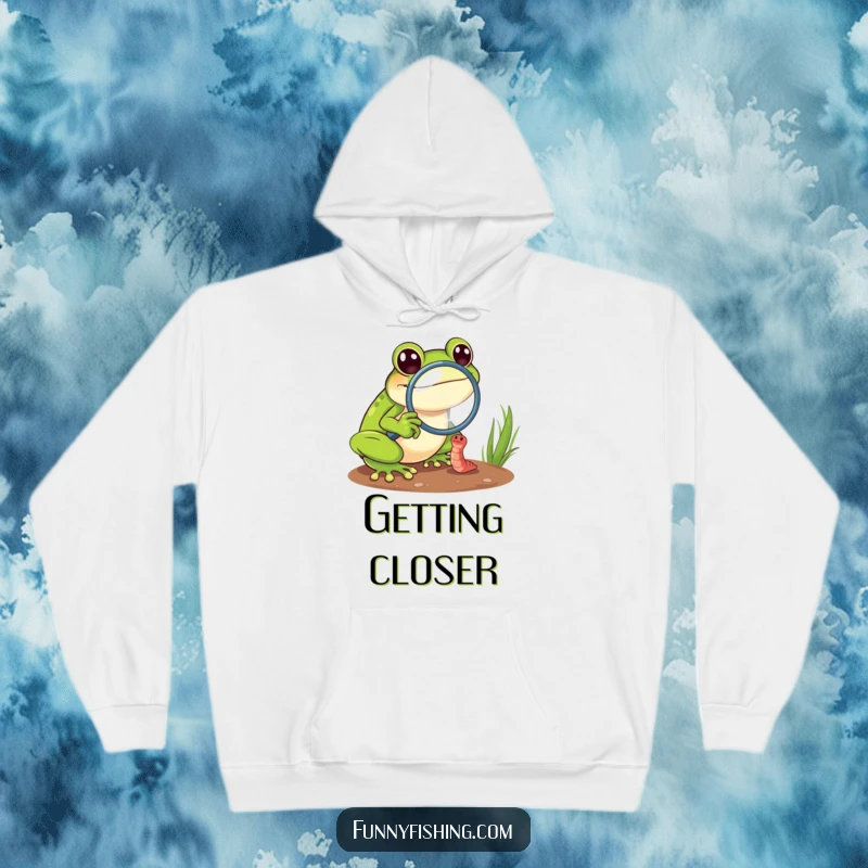 Funny frog hoodie depicting a cheerful frog with a magnifying glass intensely focused on a tiny, struggling worm, adding humor.